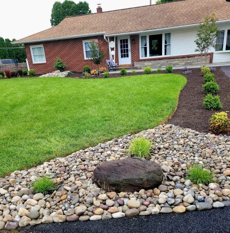 River-rock dry creek bed curving beside a lawn and planting bed in front of a brick ranch home