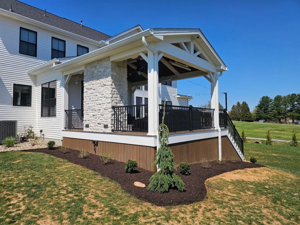 New covered porch with a deck, a weeping evergreen and a fresh planting bed in front