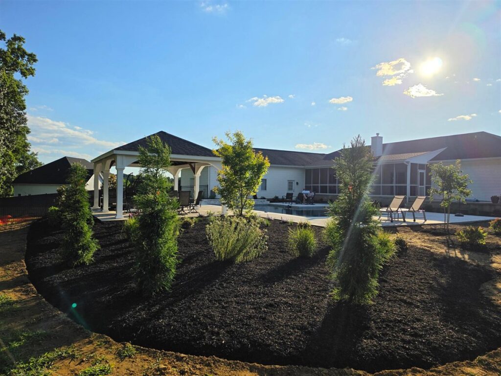 Large property with a pavilion and pool behind a big bed of evergreens and small trees